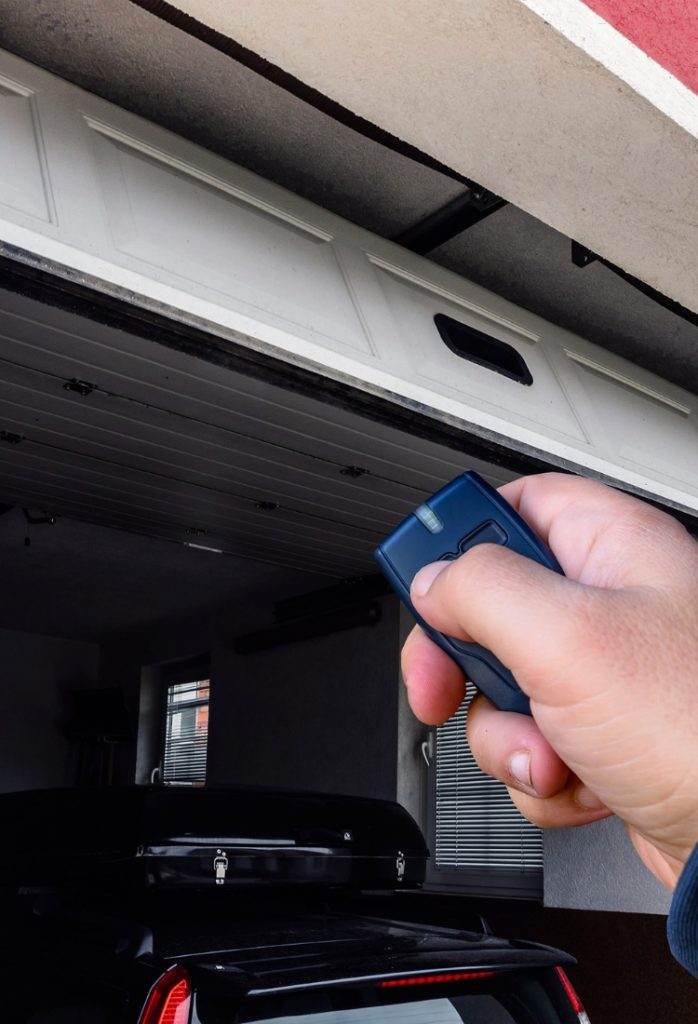 Hand operates garage door remote in residential garage during daytime Hand operates garage door remote in residential garage during daytime