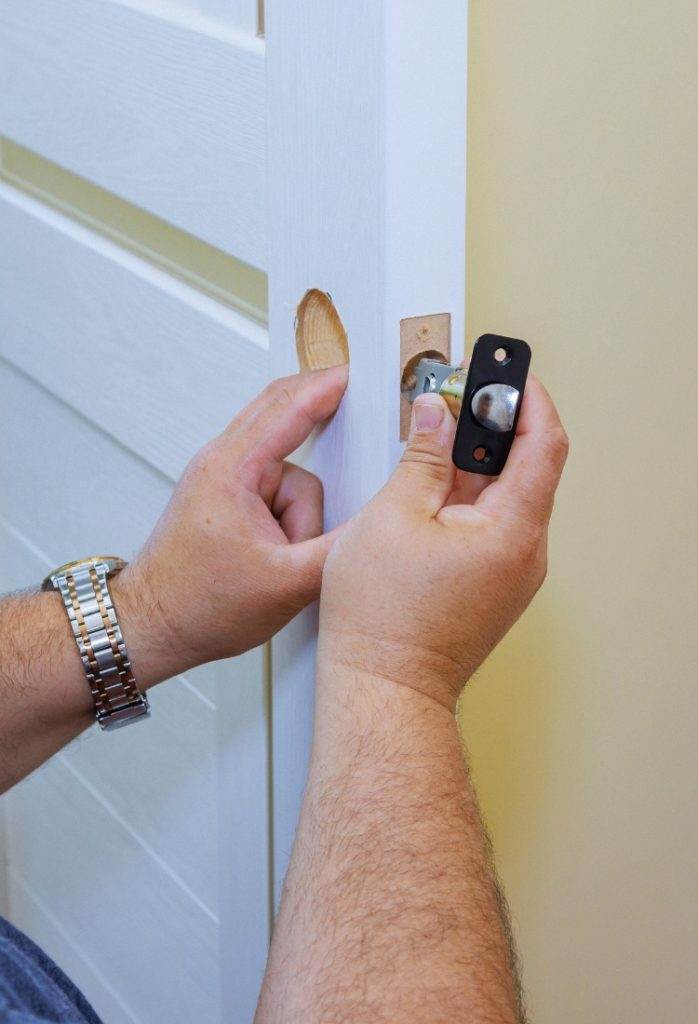 Hands installing a doorknob on a white interior door inside a home Hands installing a doorknob on a white interior door inside a home