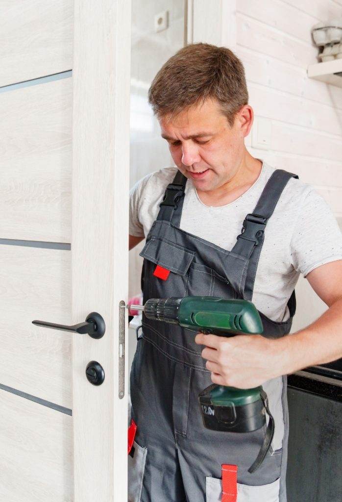Man installing a door lock using a drill in a modern home setting during daylight hours Man installing a door lock using a drill in a modern home setting during daylight hours