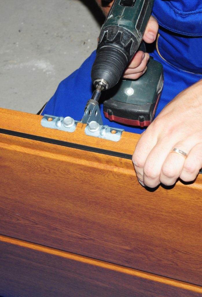 Expert craftsman installs cabinet hinge with electric drill in workshop at daytime Expert craftsman installs cabinet hinge with electric drill in workshop at daytime