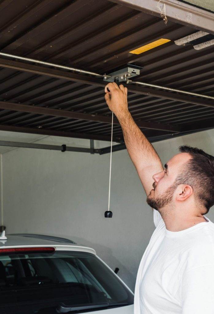 Man adjusting garage door opener in residential garage during daylight hours Man adjusting garage door opener in residential garage during daylight hours
