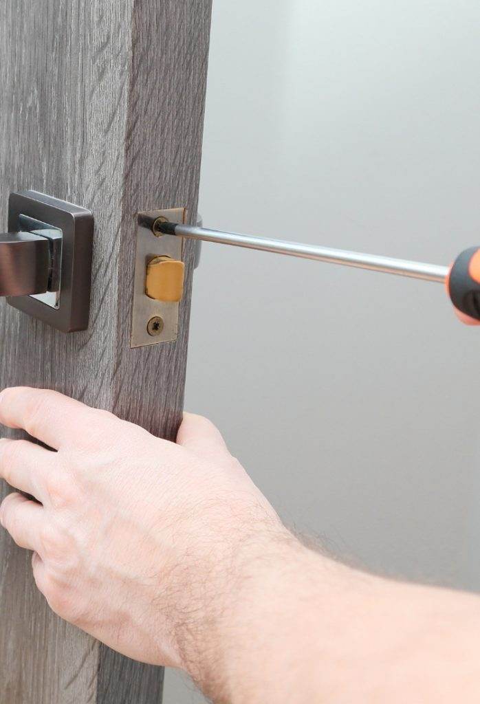 Repairing a door lock with a screwdriver in a modern interior setting during daylight hours Repairing a door lock with a screwdriver in a modern interior setting during daylight hours