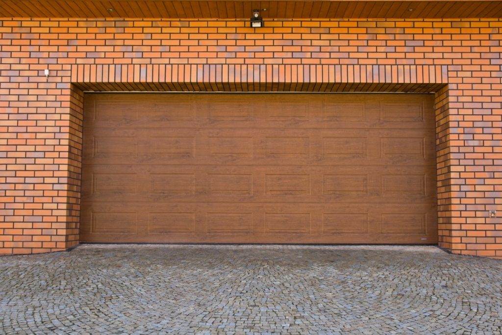 A peaceful suburban driveway leading to a closed garage surrounded by lush greenery in early fall A peaceful suburban driveway leading to a closed garage surrounded by lush greenery in early fall