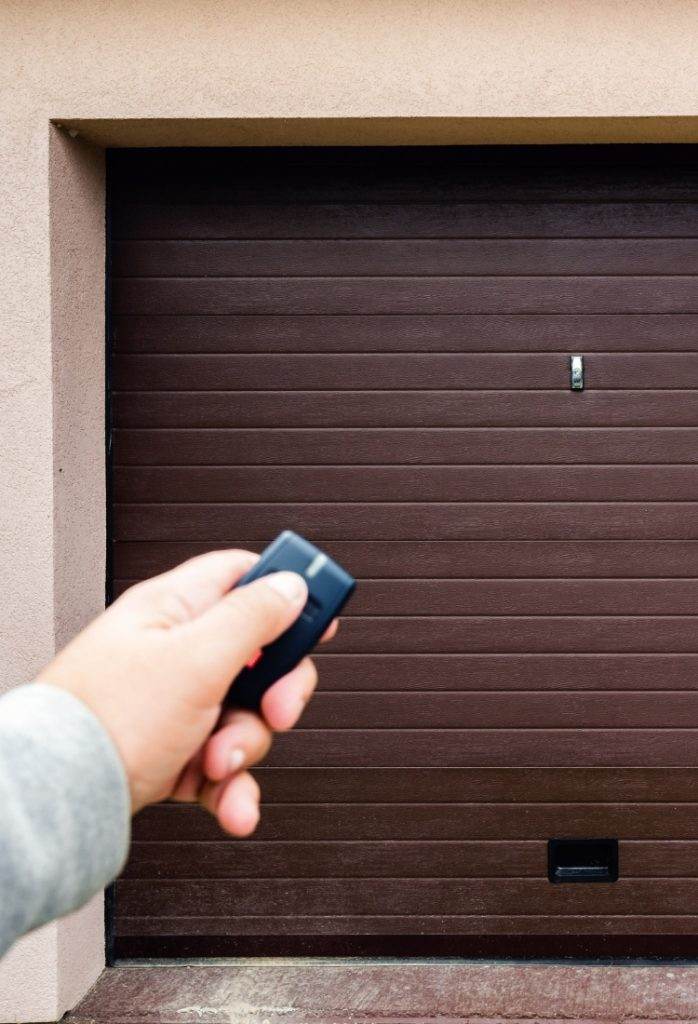 Hand holding garage door remote control outside home ready to open overhead door Hand holding garage door remote control outside home ready to open overhead door